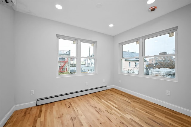 empty room featuring a wall mounted AC, a wealth of natural light, a baseboard radiator, and hardwood / wood-style flooring