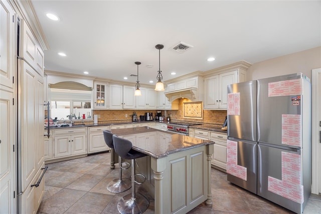 kitchen with a kitchen breakfast bar, hanging light fixtures, dark stone countertops, a kitchen island, and stainless steel refrigerator