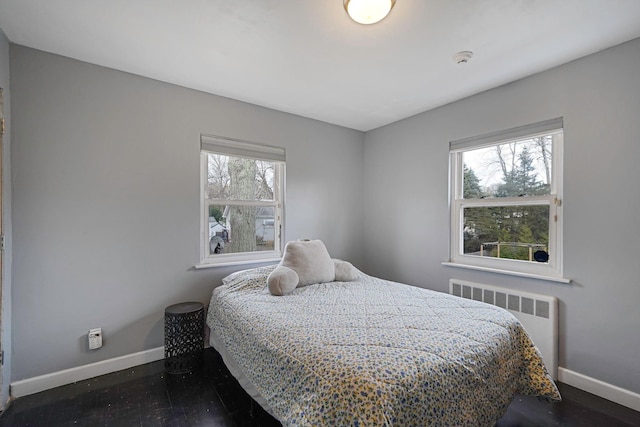 bedroom with multiple windows, radiator heating unit, and dark hardwood / wood-style flooring