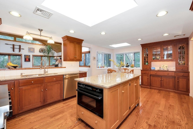 kitchen featuring black oven, a skylight, sink, stainless steel dishwasher, and light stone countertops