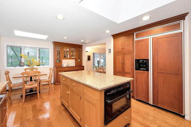 kitchen with light stone counters, light wood-type flooring, paneled built in fridge, a kitchen island, and oven