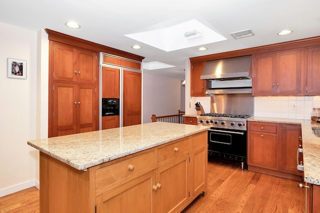 kitchen with wall chimney range hood, light hardwood / wood-style flooring, a center island, premium appliances, and light stone countertops