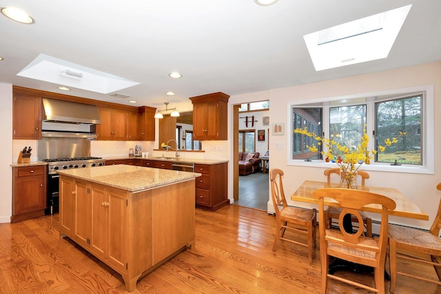 kitchen featuring wall chimney exhaust hood, a center island, a skylight, appliances with stainless steel finishes, and light stone countertops