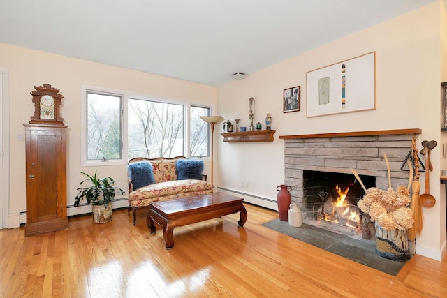 living area with a stone fireplace, hardwood / wood-style flooring, and baseboard heating