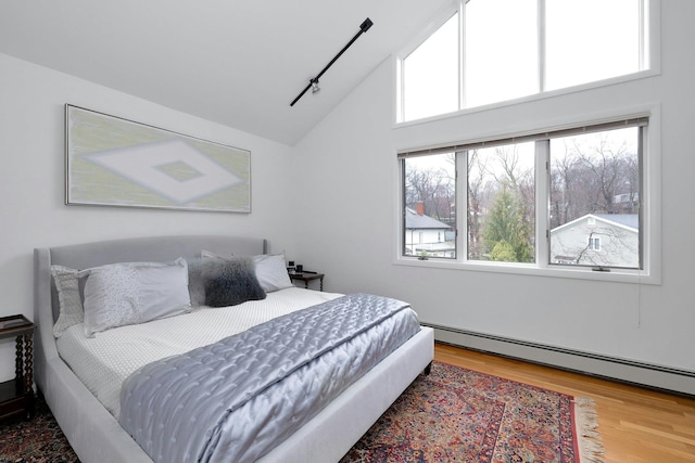 bedroom with hardwood / wood-style flooring, vaulted ceiling, rail lighting, and a baseboard heating unit