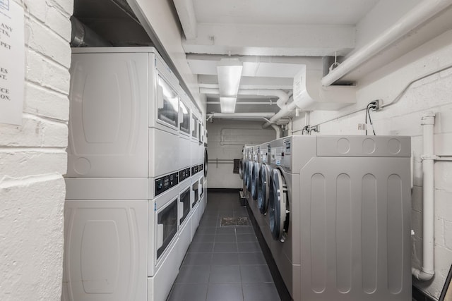 laundry room featuring dark tile patterned flooring and stacked washer / drying machine