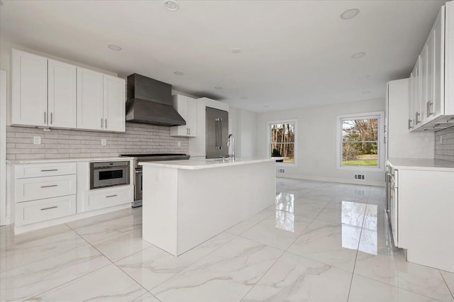 kitchen featuring appliances with stainless steel finishes, tasteful backsplash, white cabinetry, and wall chimney exhaust hood