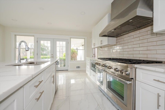 kitchen featuring white cabinetry, sink, light stone countertops, wall chimney range hood, and appliances with stainless steel finishes