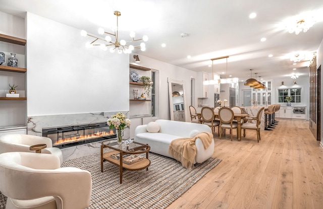 living room with built in features, light wood-type flooring, a fireplace, and an inviting chandelier