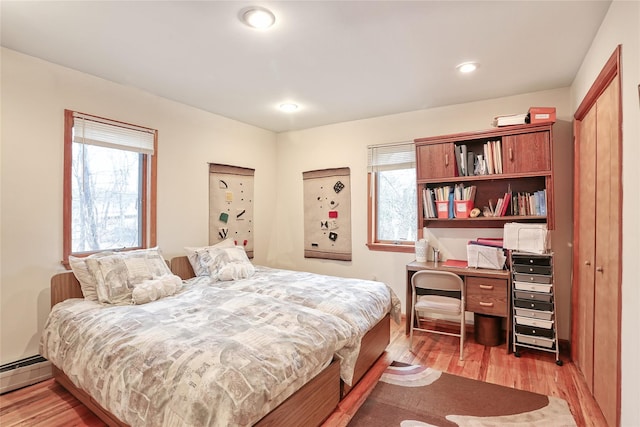 bedroom featuring a closet, baseboard heating, and light hardwood / wood-style flooring