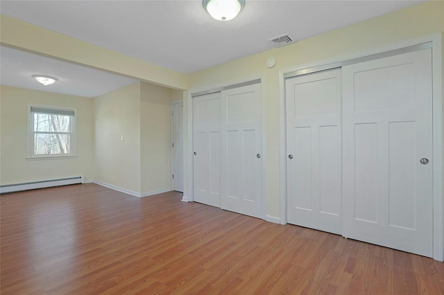 unfurnished bedroom with light hardwood / wood-style floors, baseboard heating, and multiple closets