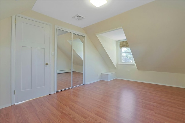 additional living space with a baseboard heating unit, light wood-type flooring, and vaulted ceiling