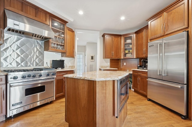 kitchen with a center island, built in appliances, decorative backsplash, light wood-type flooring, and extractor fan