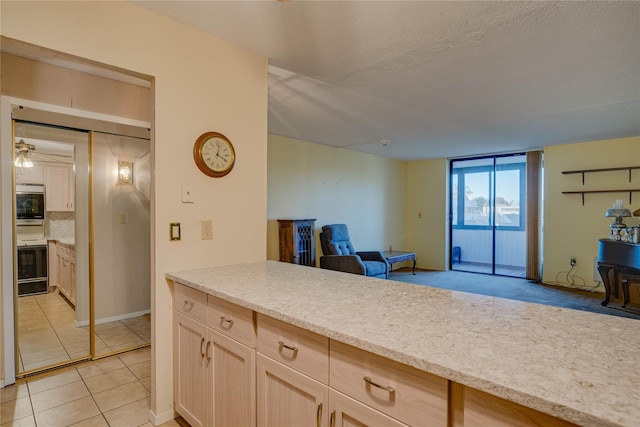 kitchen with light brown cabinetry, stainless steel oven, light tile patterned floors, wall oven, and a textured ceiling