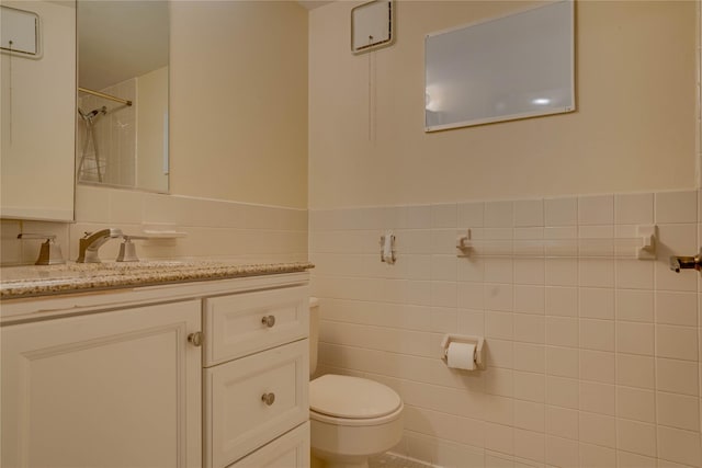 bathroom featuring walk in shower, vanity, toilet, and tile walls