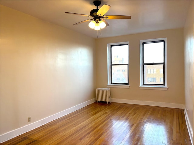 unfurnished room with hardwood / wood-style flooring, ceiling fan, and radiator heating unit