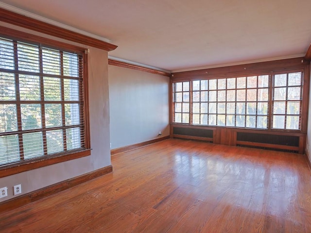 empty room featuring radiator, a wealth of natural light, hardwood / wood-style floors, and crown molding