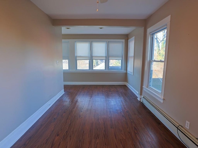 spare room featuring baseboard heating and dark hardwood / wood-style floors