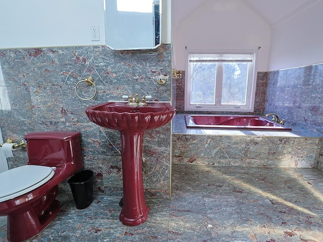 bathroom featuring sink, tiled tub, tile walls, toilet, and lofted ceiling