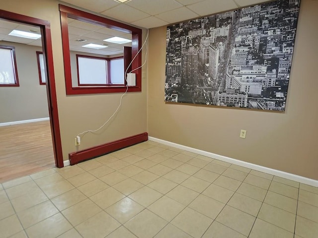 spare room featuring a paneled ceiling, light tile patterned floors, and a healthy amount of sunlight