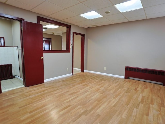 empty room with a drop ceiling, light wood-type flooring, and radiator heating unit