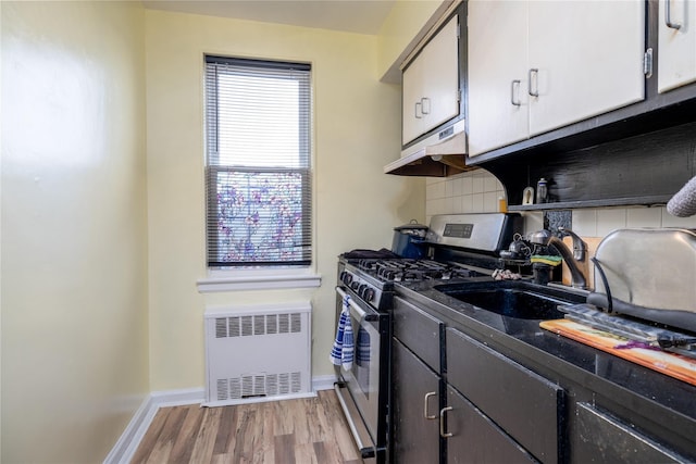 kitchen with decorative backsplash, gas stove, sink, light hardwood / wood-style flooring, and radiator heating unit