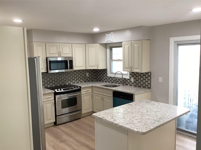 kitchen with decorative backsplash, appliances with stainless steel finishes, light stone countertops, sink, and light hardwood / wood-style flooring