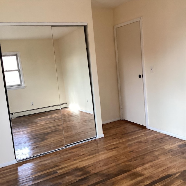 unfurnished bedroom featuring baseboard heating, a closet, and dark hardwood / wood-style flooring