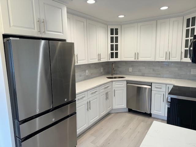 kitchen with white cabinets, sink, light wood-type flooring, tasteful backsplash, and stainless steel appliances