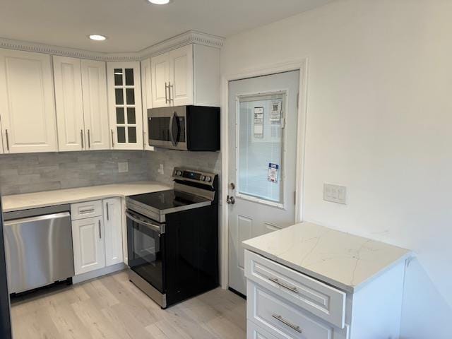 kitchen with white cabinets, appliances with stainless steel finishes, decorative backsplash, and light hardwood / wood-style flooring