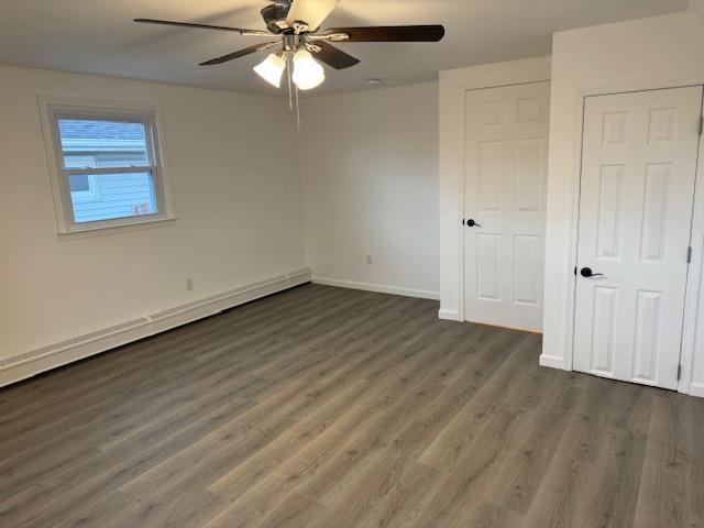 unfurnished bedroom featuring ceiling fan, dark hardwood / wood-style flooring, and a baseboard heating unit