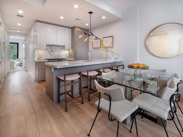 kitchen with kitchen peninsula, sink, decorative light fixtures, light hardwood / wood-style flooring, and white cabinets