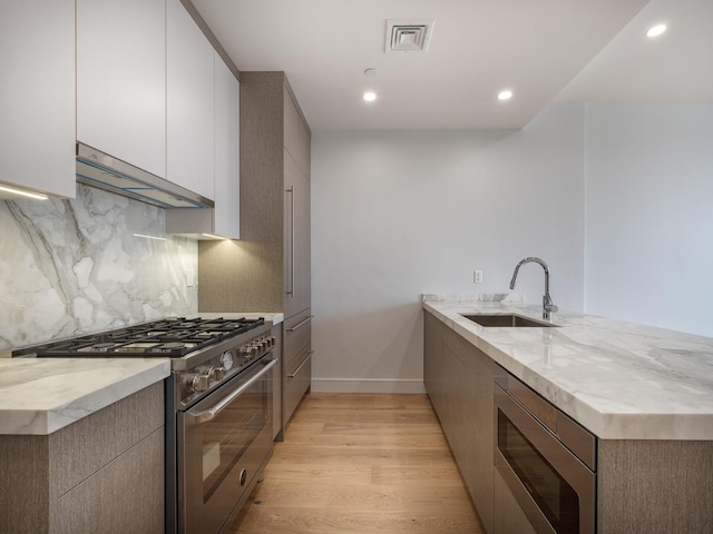 kitchen with ventilation hood, sink, light hardwood / wood-style flooring, kitchen peninsula, and stainless steel appliances