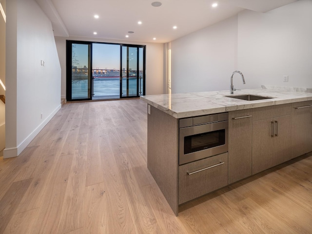 kitchen with light stone countertops, light hardwood / wood-style floors, stainless steel microwave, and sink