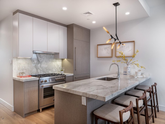 kitchen featuring decorative light fixtures, kitchen peninsula, high end stainless steel range oven, and light hardwood / wood-style flooring