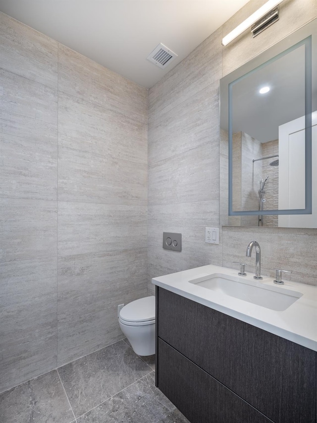 bathroom featuring vanity, toilet, tile walls, and walk in shower