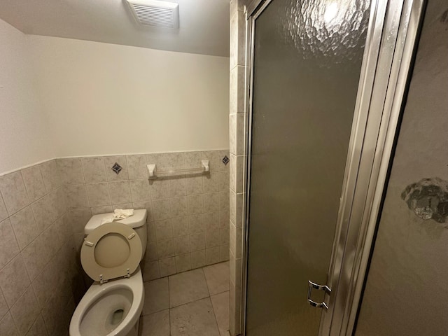 bathroom with tile patterned floors, a shower with door, toilet, and tile walls