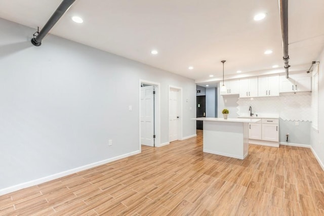 kitchen with white cabinets, sink, light wood-type flooring, and hanging light fixtures