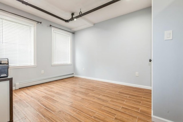 empty room with a wealth of natural light, light hardwood / wood-style flooring, and a baseboard heating unit