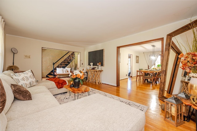 living room with light wood-type flooring, ornamental molding, and an inviting chandelier