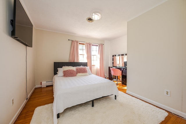 bedroom with ornamental molding, a baseboard radiator, and hardwood / wood-style flooring