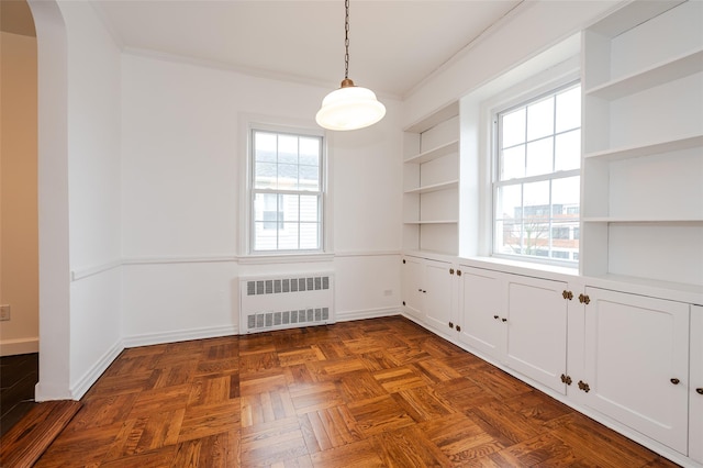 unfurnished dining area featuring radiator heating unit, built in features, dark parquet flooring, and crown molding