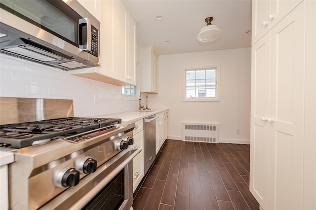 kitchen featuring radiator, sink, dark hardwood / wood-style floors, white cabinets, and appliances with stainless steel finishes