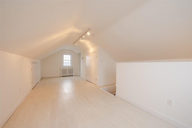 additional living space featuring radiator, vaulted ceiling, and light wood-type flooring