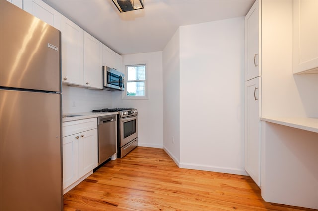 kitchen with decorative backsplash, white cabinetry, stainless steel appliances, and light hardwood / wood-style floors