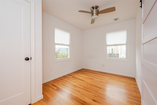 spare room with ceiling fan, a barn door, and light wood-type flooring