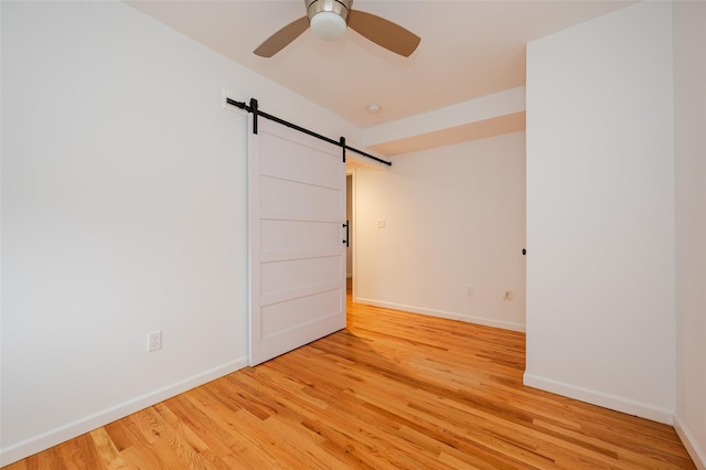 unfurnished room featuring ceiling fan, a barn door, and light hardwood / wood-style floors