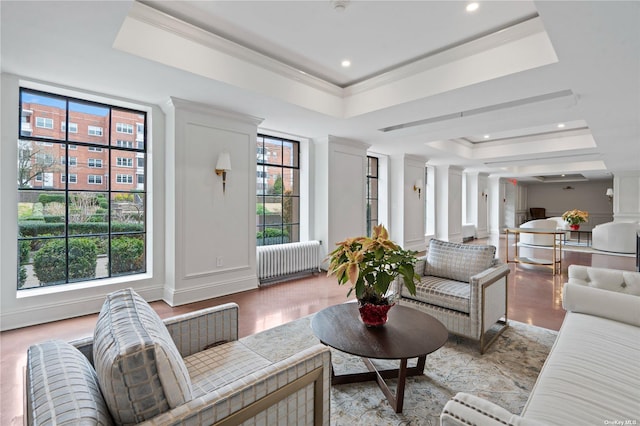 living room with radiator, decorative columns, light hardwood / wood-style floors, a raised ceiling, and crown molding