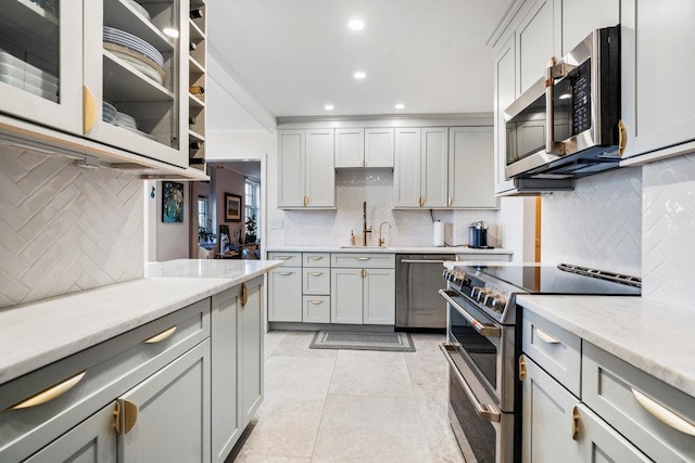 kitchen featuring light stone counters, decorative backsplash, gray cabinetry, and appliances with stainless steel finishes