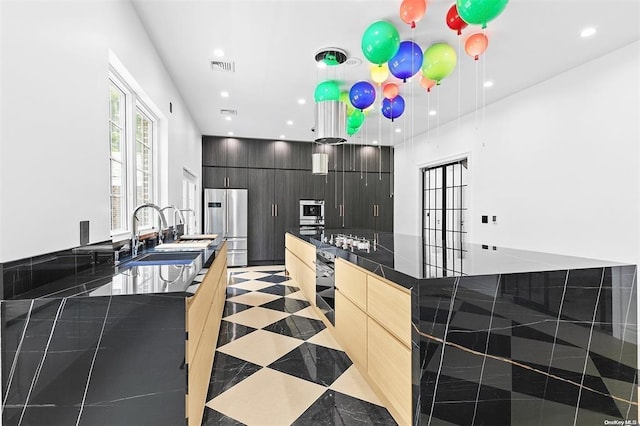 kitchen with sink, hanging light fixtures, light brown cabinetry, high end refrigerator, and oven